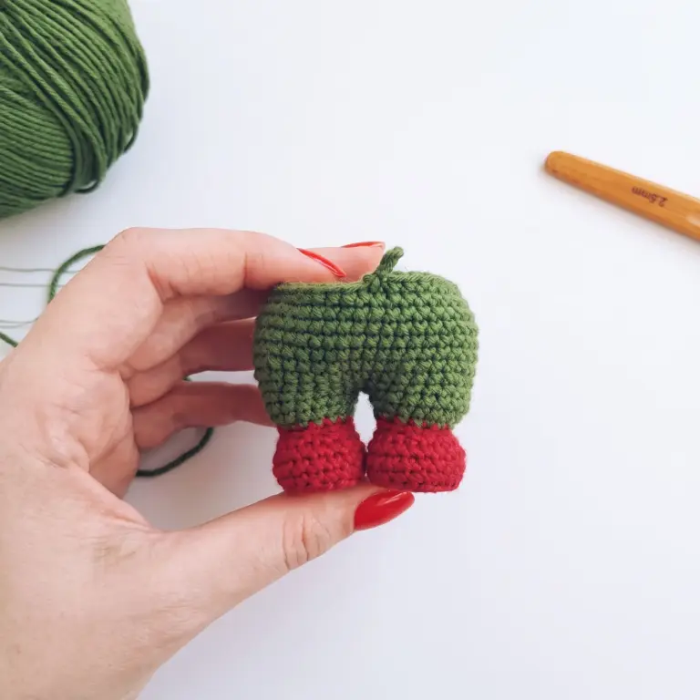 Two crocheted gnome legs joined together in green and red, held in a hand