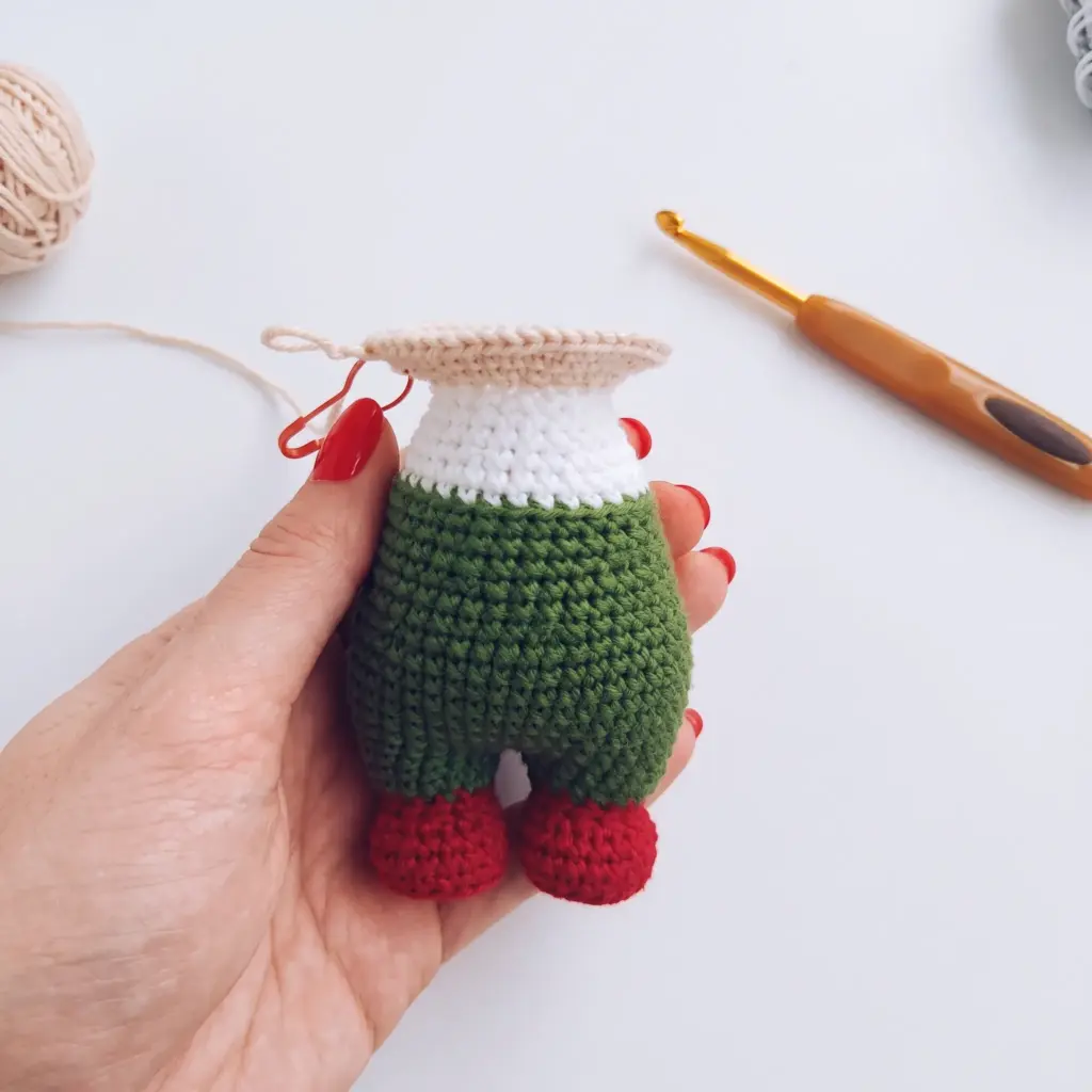Crocheted gnome body with green overalls, white belt band, and red boots, ready for the head