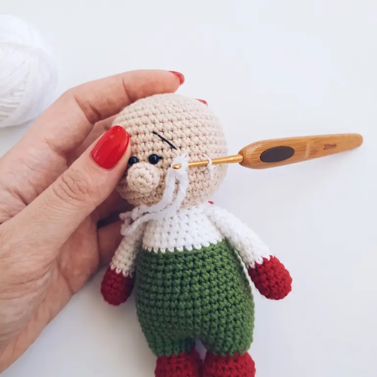 Attaching fuzzy white beard strands to the gnome's face with a crochet hook